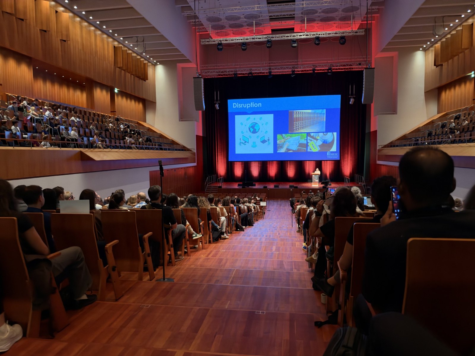 Conference participants in Freiburg's Konzerthaus, facing the stage and presentation screen.